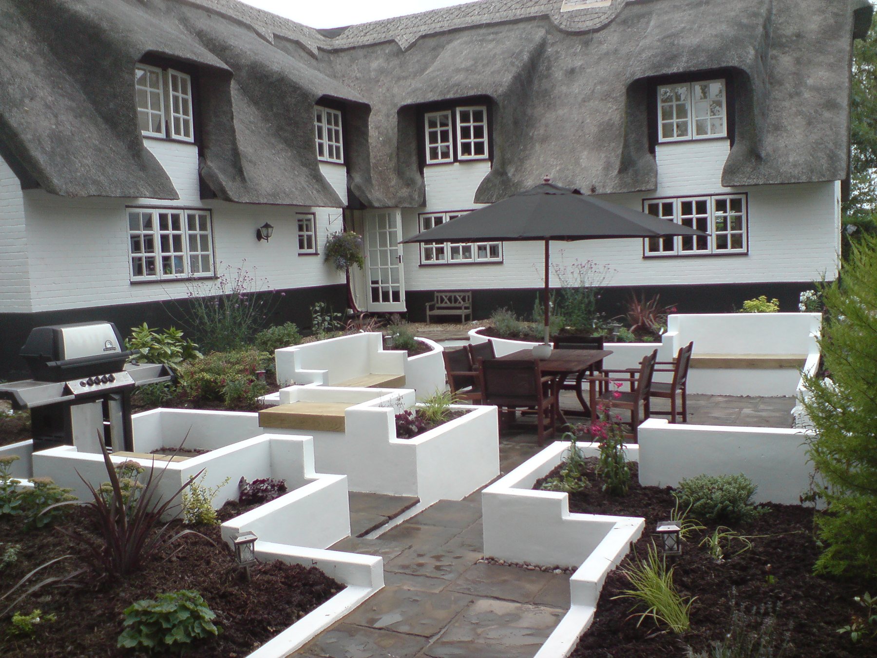 After: A plain lawn behind a thatched cottage, turned into a terrace with rendered raised beds.
