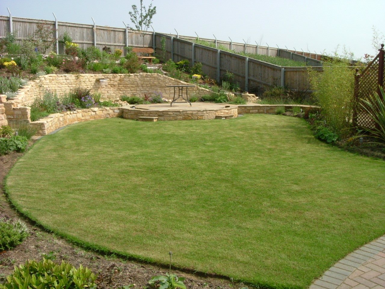 After: A bare plot with the diggers on site, finished as a round lawn below curved stone walls.