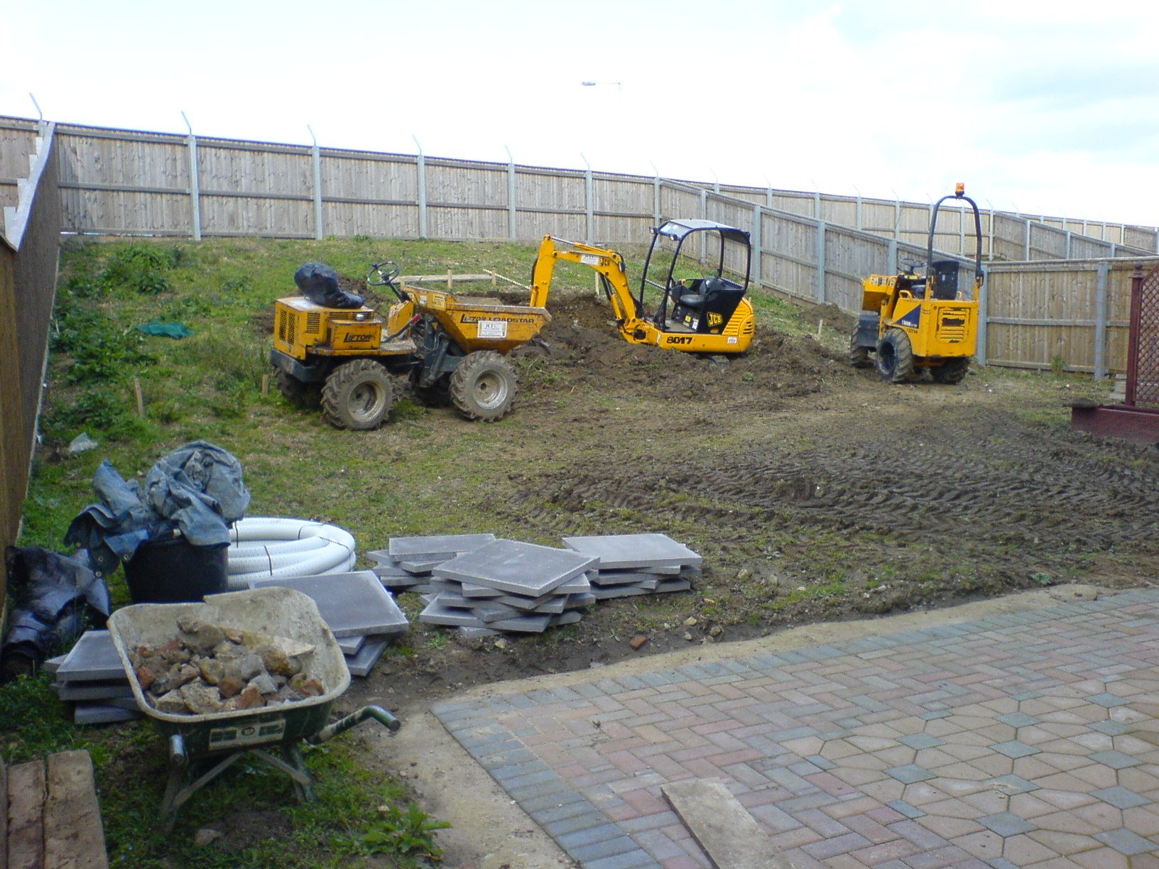 Before: A bare plot with the diggers on site, finished as a round lawn below curved stone walls.