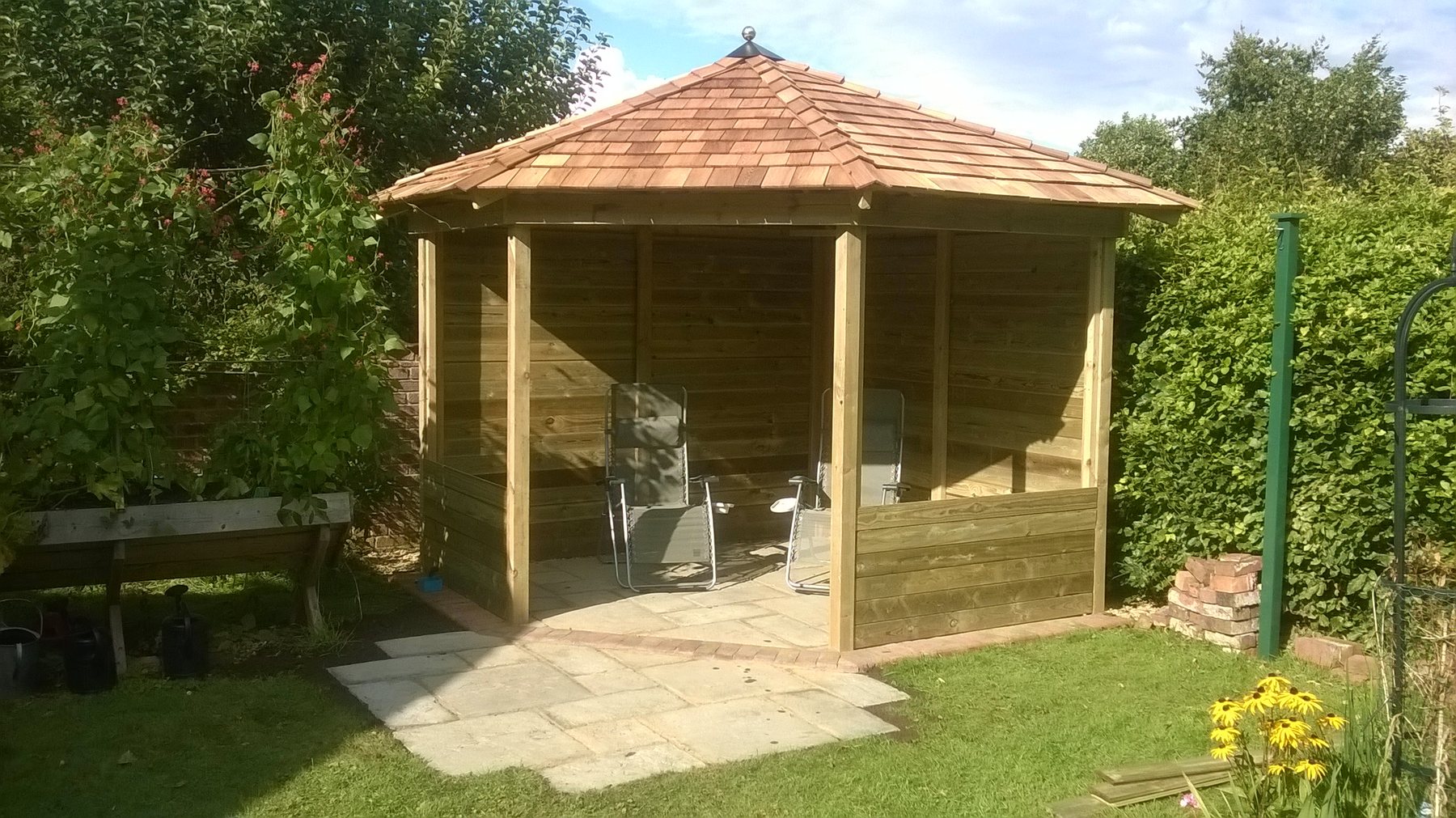 Timber gazebo with a cedar shingle roof in a planted garden