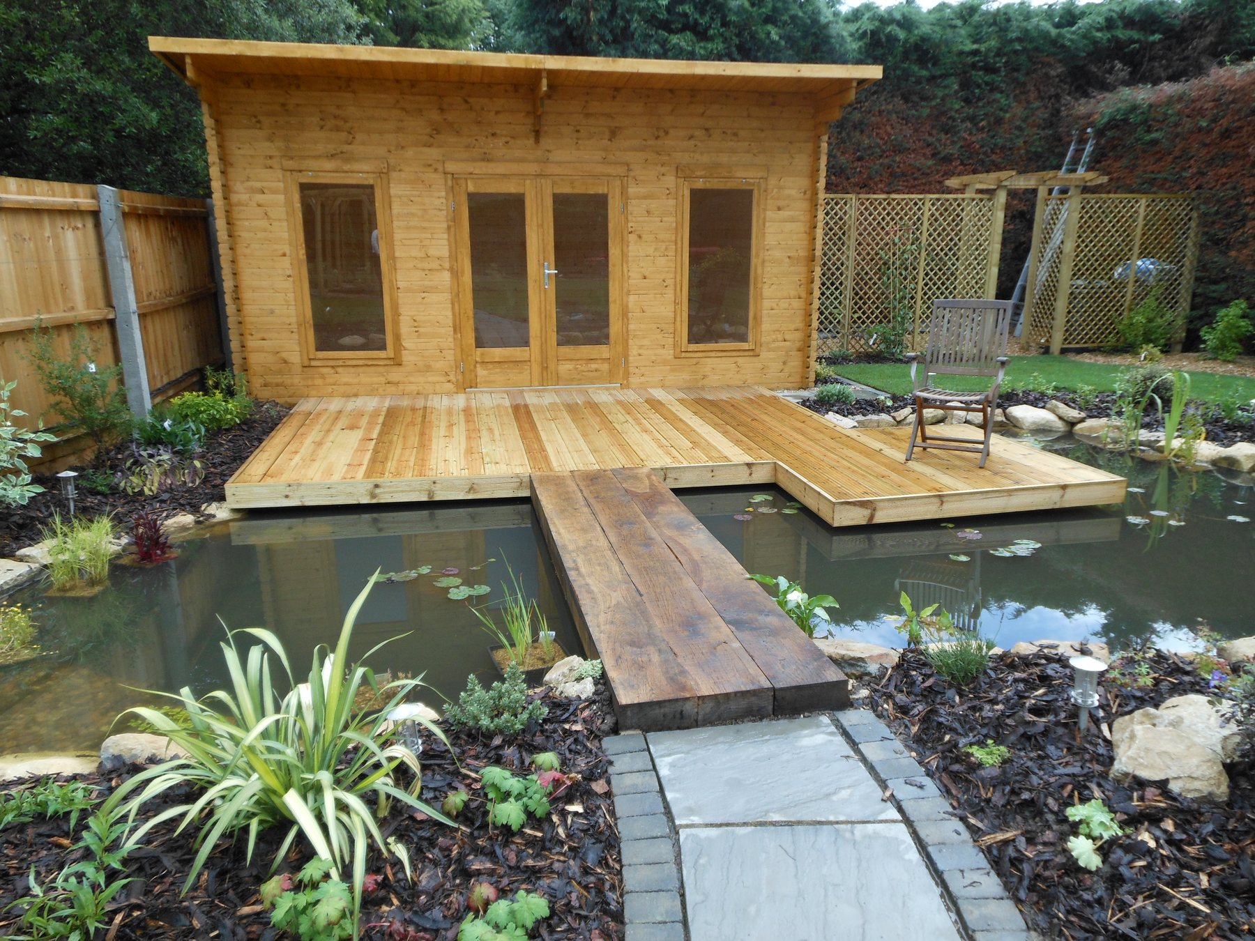 Garden room with a deck and a timber walkway across a pond