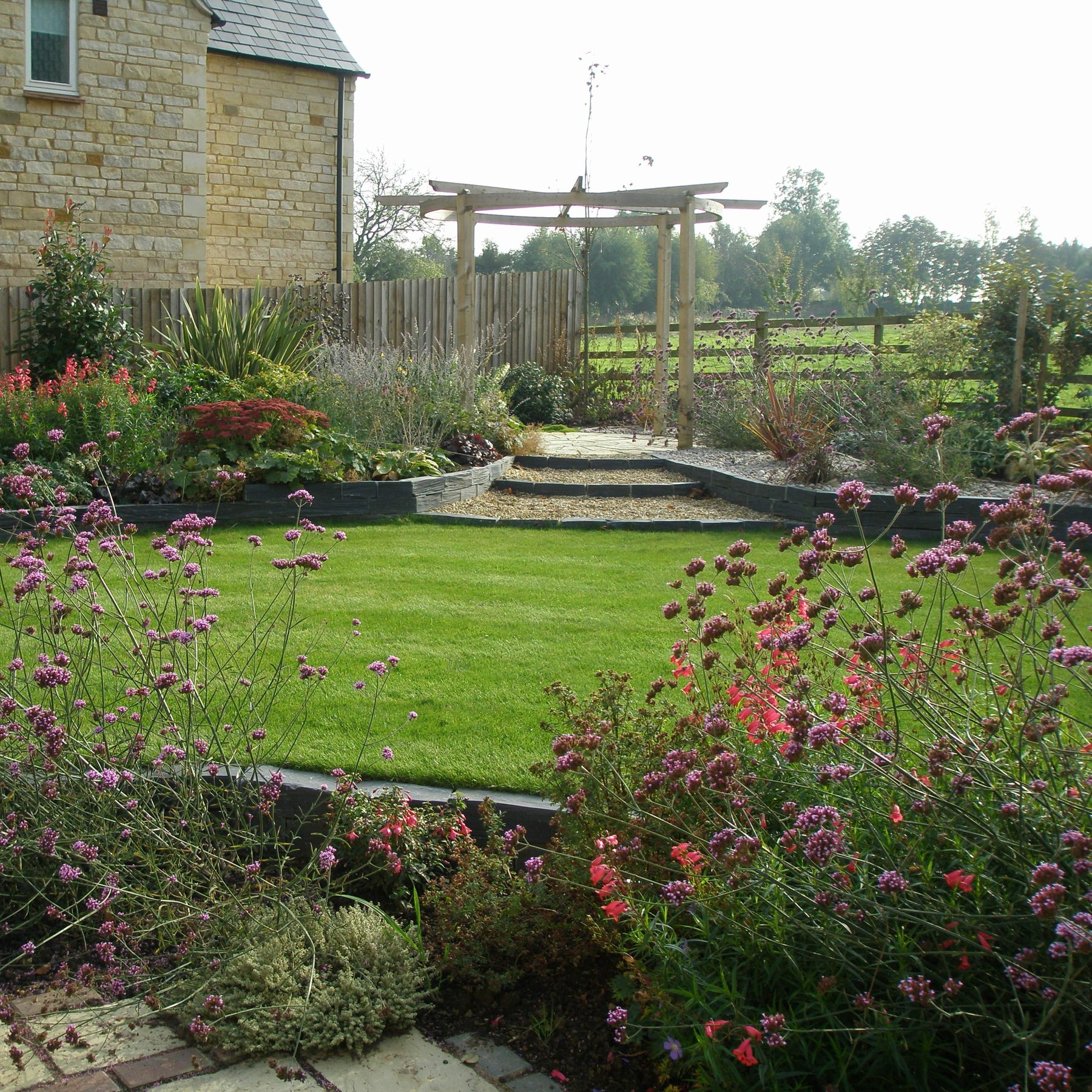 Lawn and flowering borders with a pergola beyond