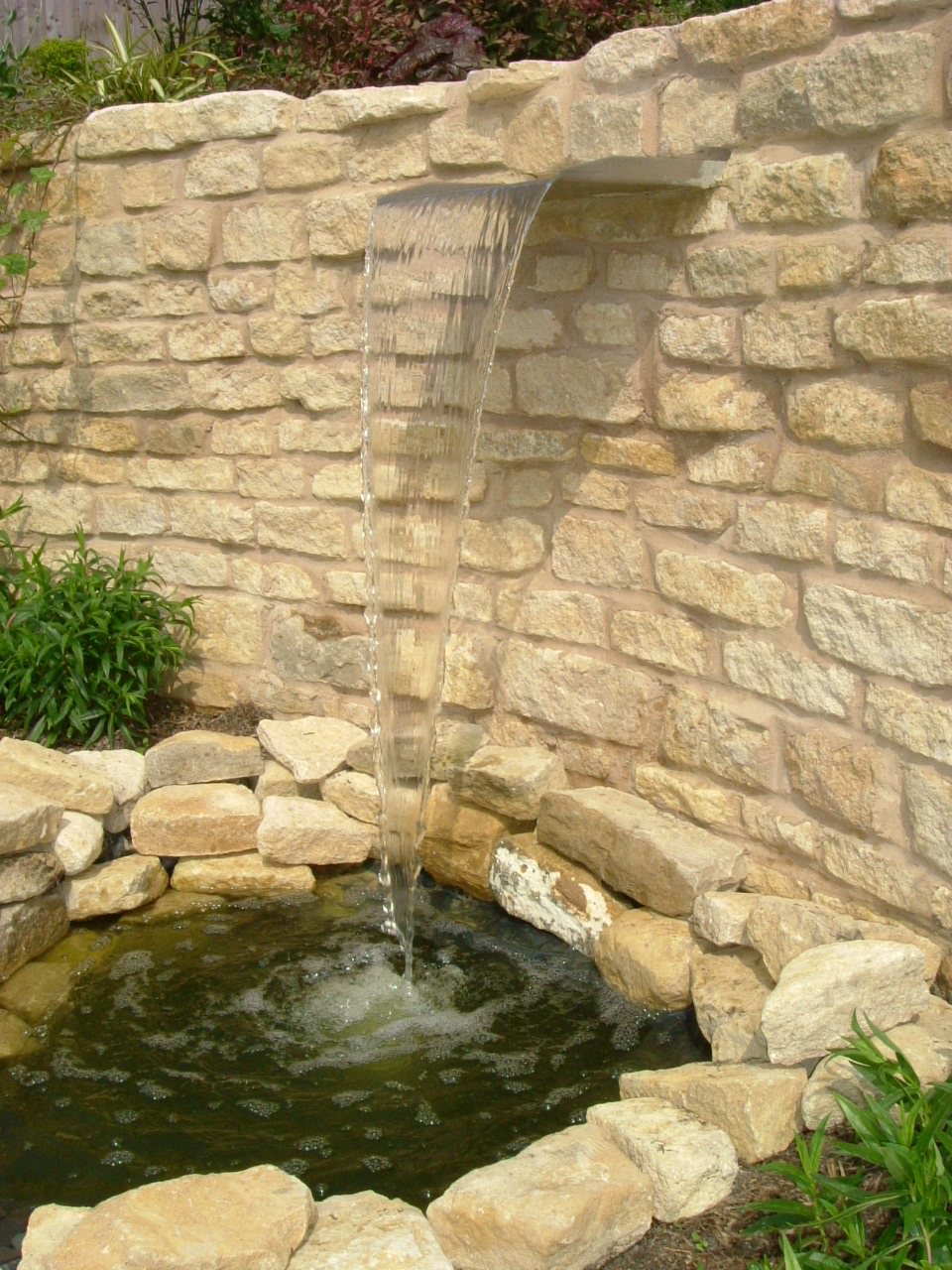 Stone wall with a water blade falling into a pond
