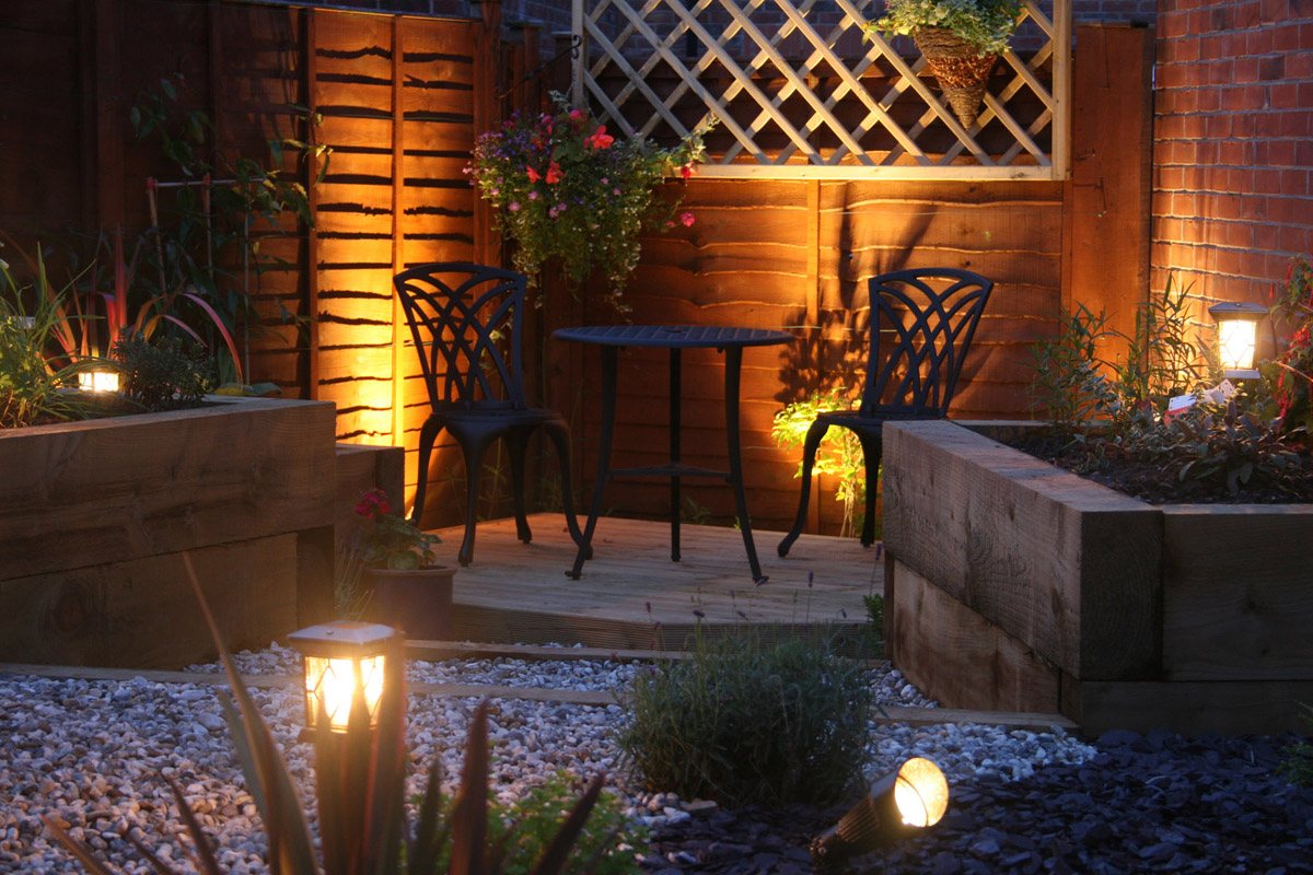Garden lighting at dusk around sleeper beds and a bistro table