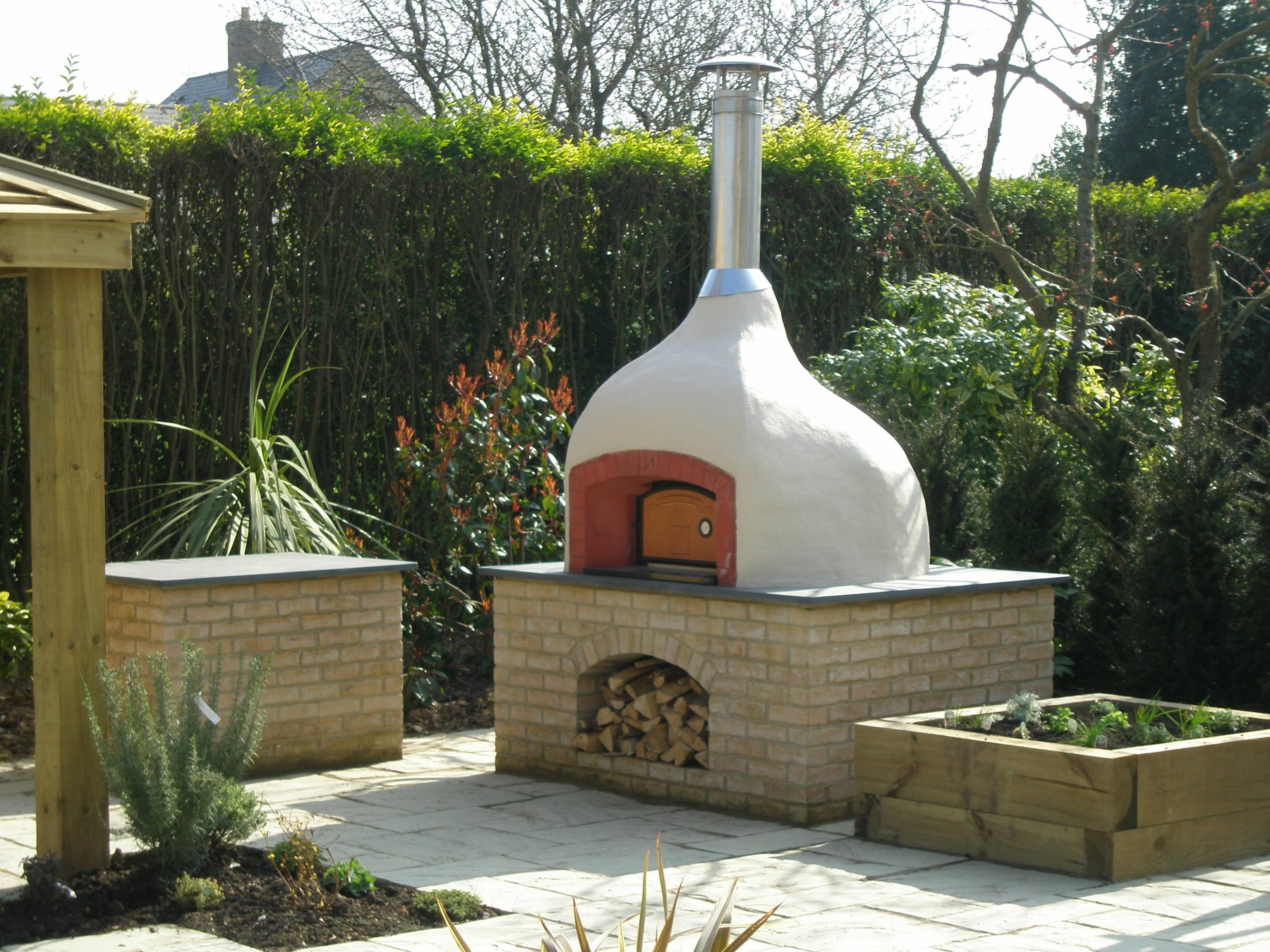 Wood-fired pizza oven on a brick base with a log store