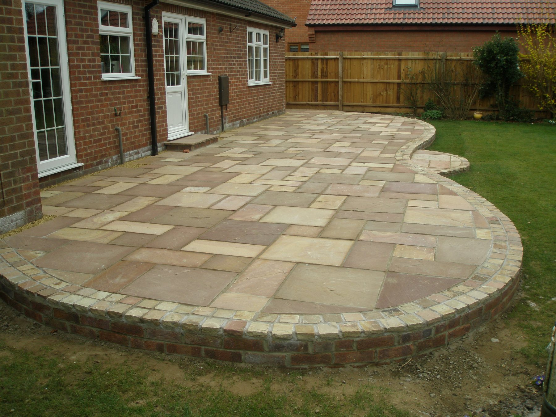 Curved sandstone patio with a brick border
