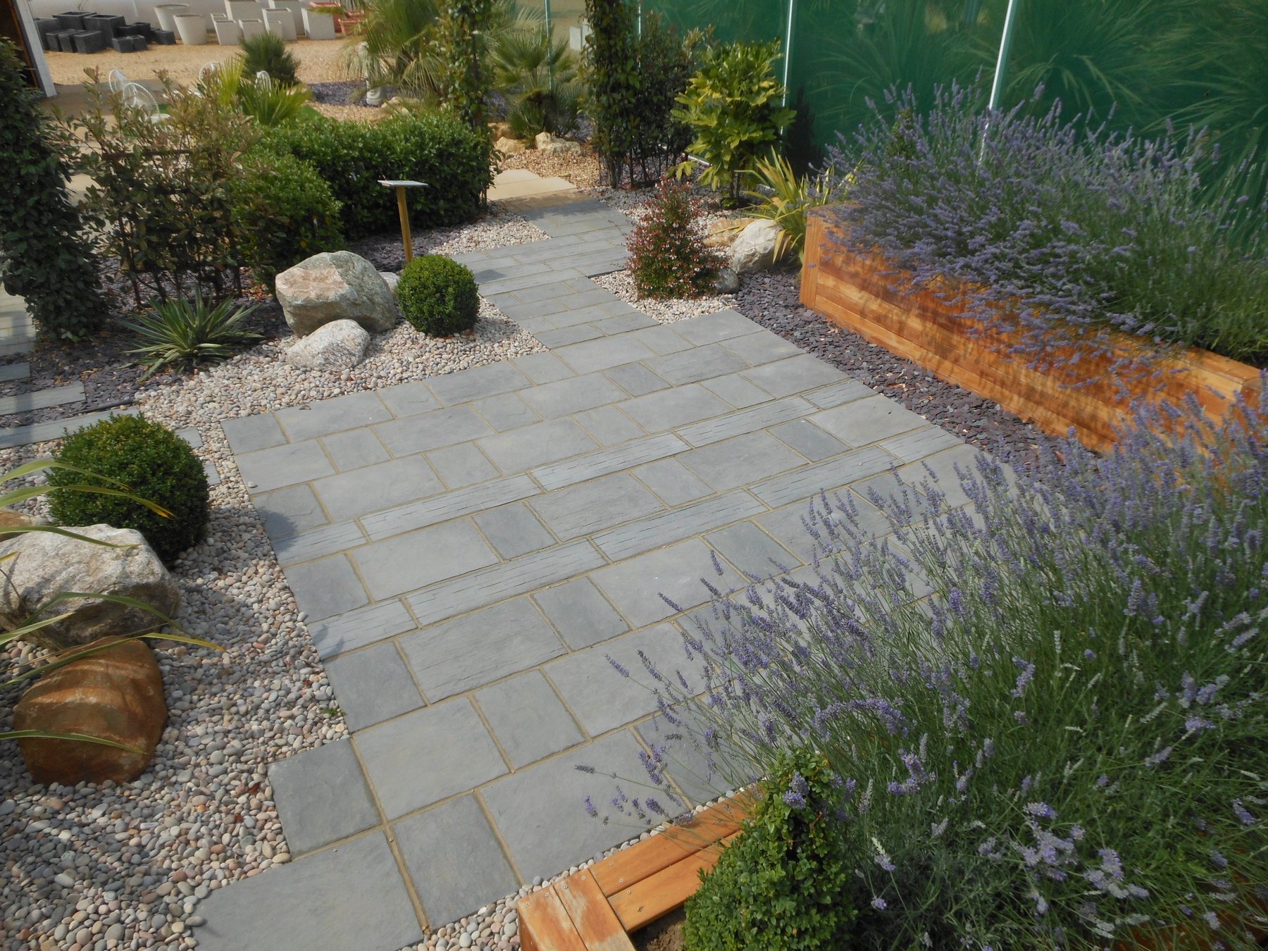 Contemporary show garden with grey slate paving, hardwood faced planters and boulders