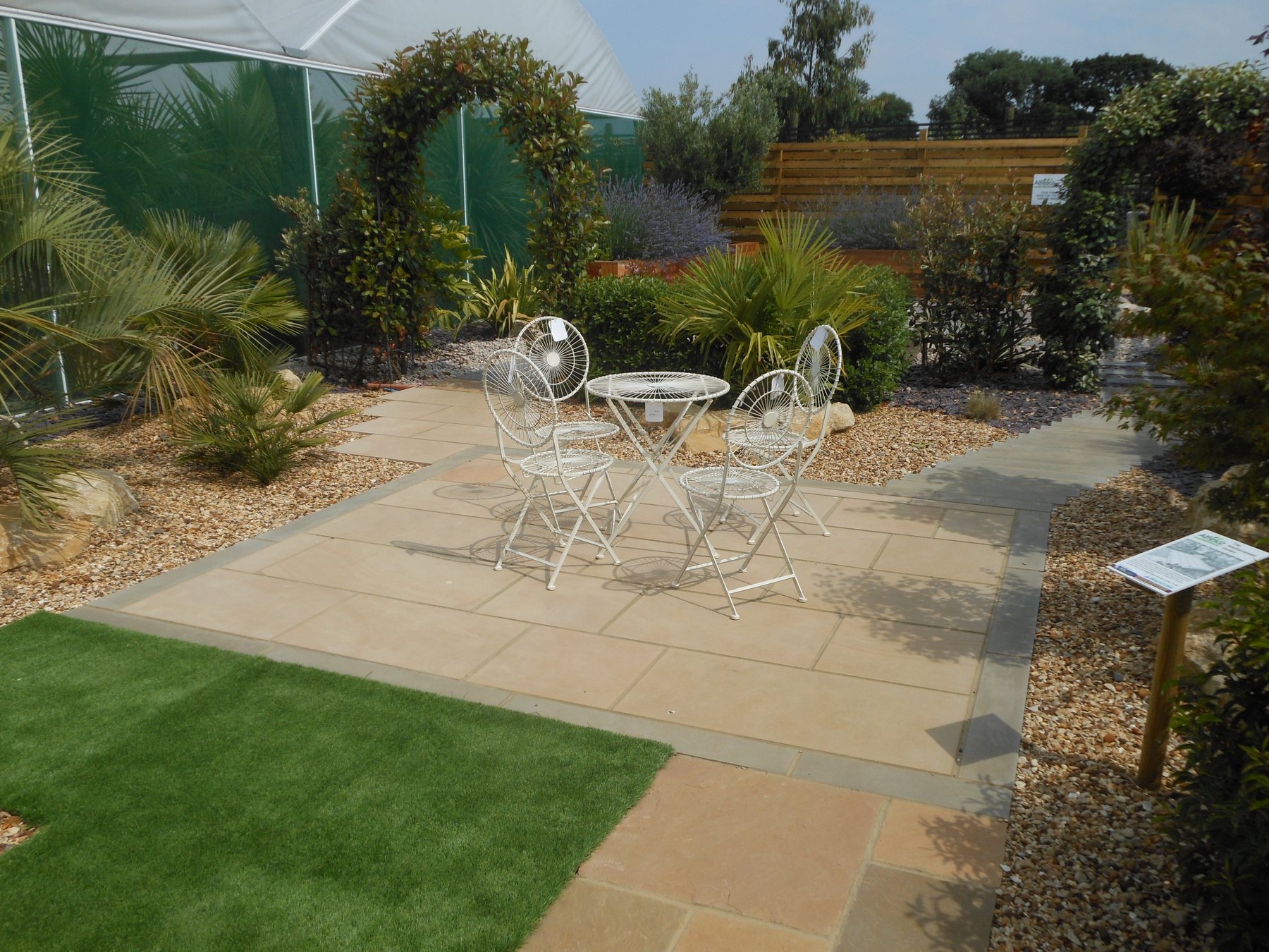 Mediterranean show garden with honed sandstone paving, palms and a white bistro set