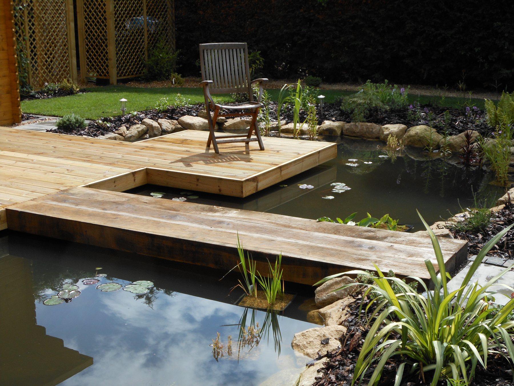 Timber deck floating over a planted pond with water lilies