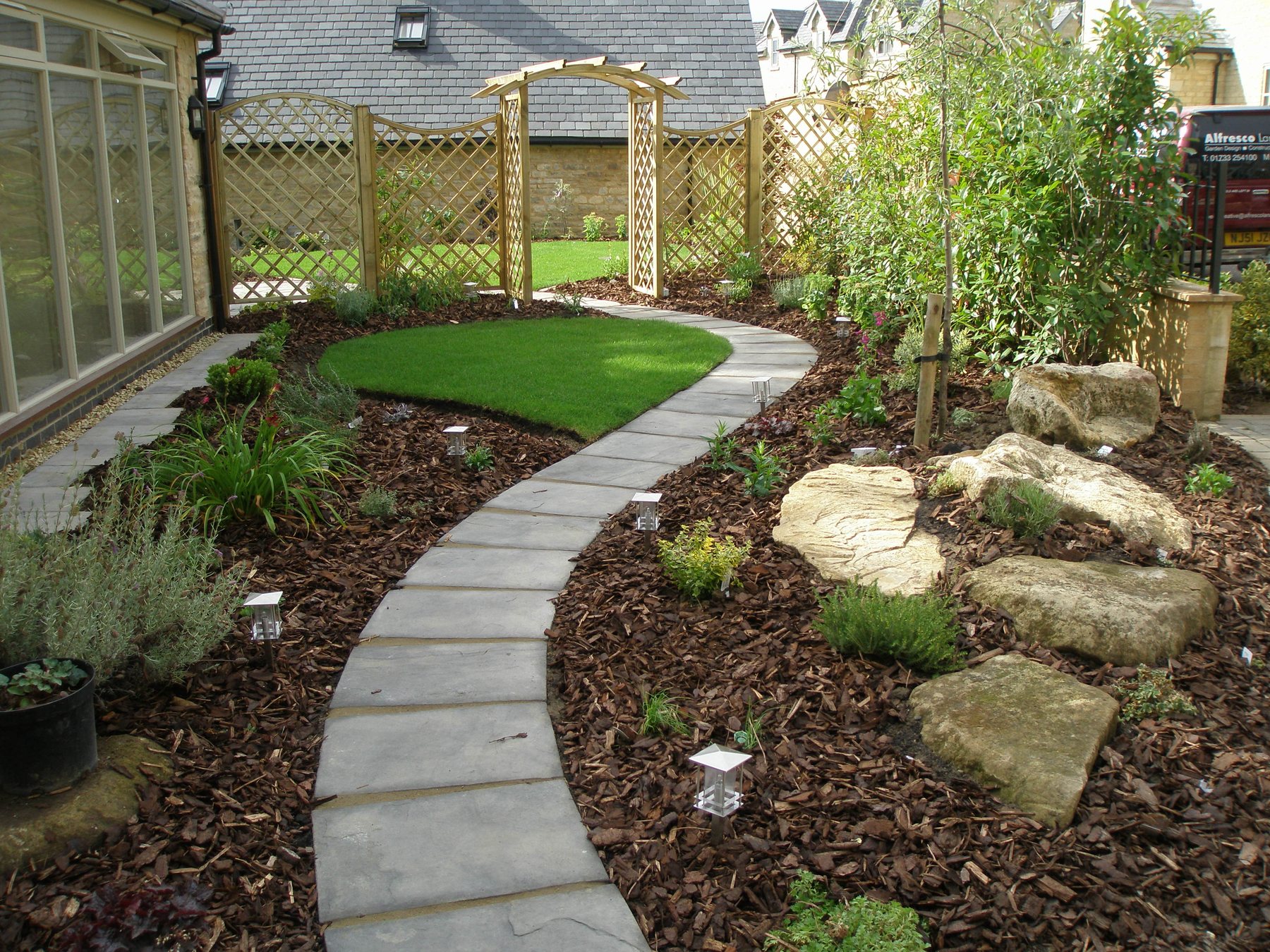Curved stone path with a trellis arch and screens
